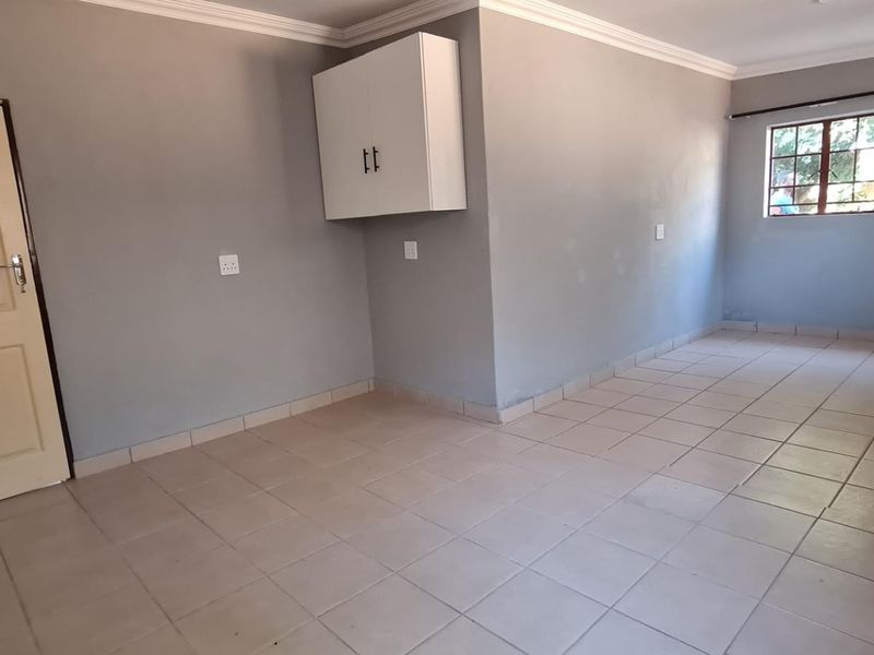 An empty, neutrally painted living area featuring tiled flooring, a wall-mounted storage cabinet, and classic cove cornicing.