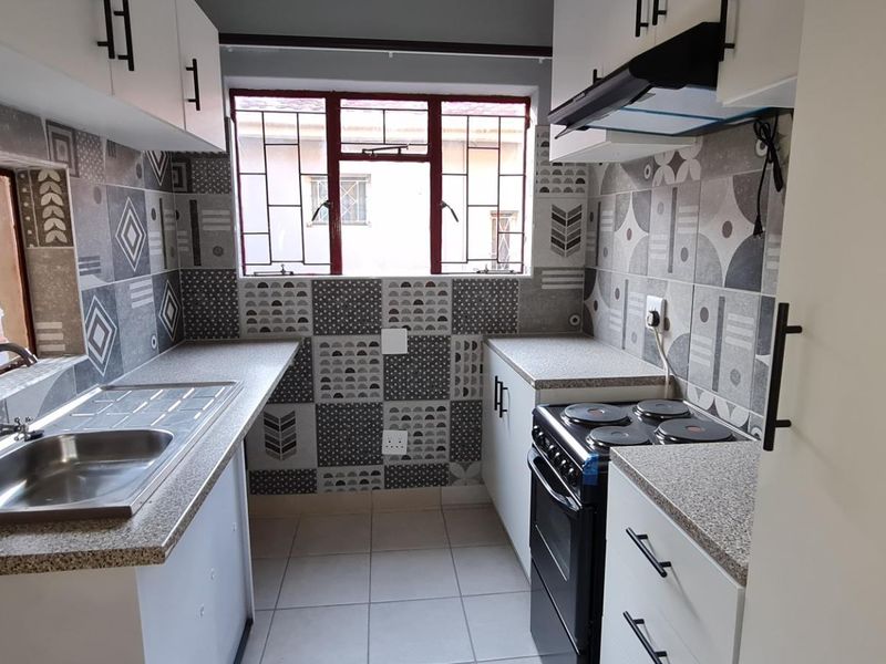 A clean, modern kitchen featuring patterned tiled splashbacks, white cabinetry, laminate countertops, and a functional layout with a built-in stove and extractor fan.