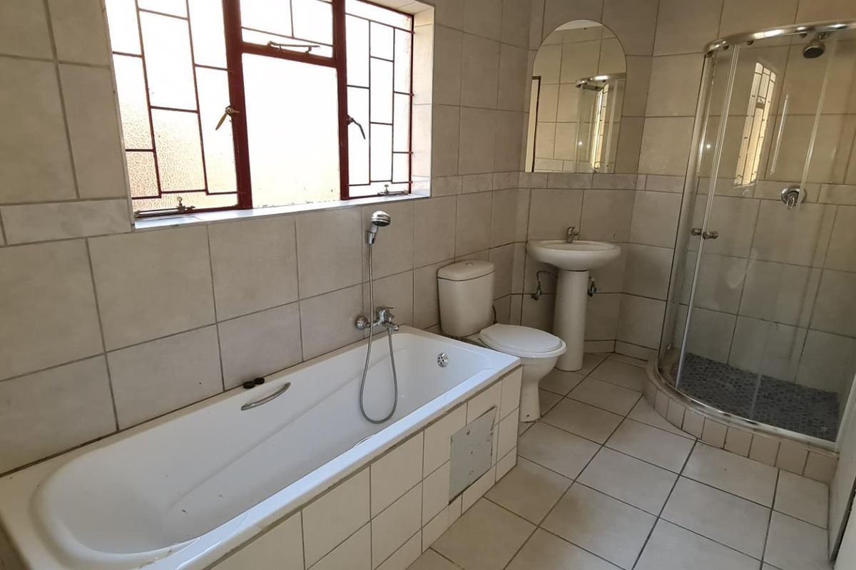 A functional bathroom featuring a built-in bathtub, pedestal basin, toilet, and a separate corner shower enclosure with tiled finishes throughout.
