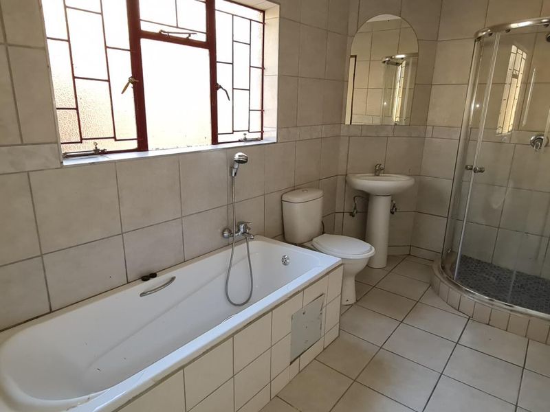 A functional bathroom featuring a built-in bathtub, pedestal basin, toilet, and a separate corner shower enclosure with tiled finishes throughout.