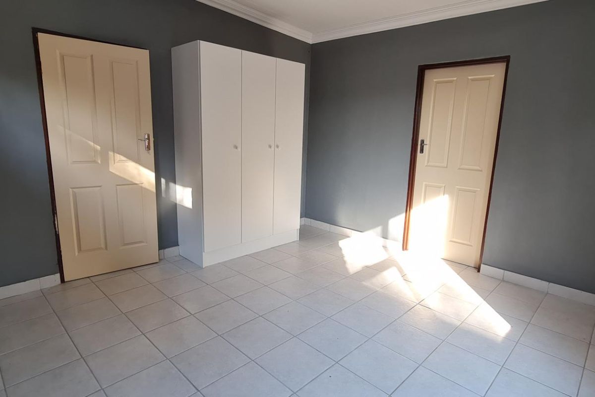 A clean, empty bedroom featuring neutral grey walls, tiled flooring, and a built-in white wardrobe, offering a blank canvas for personalization.