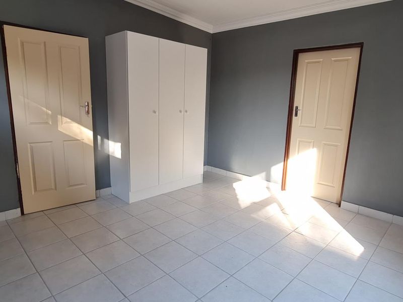 A clean, empty bedroom featuring neutral grey walls, tiled flooring, and a built-in white wardrobe, offering a blank canvas for personalization.