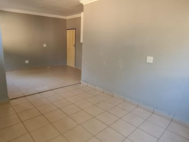 An empty open-plan living area featuring neutral tiled flooring and coved cornicing, providing a blank canvas for interior design.