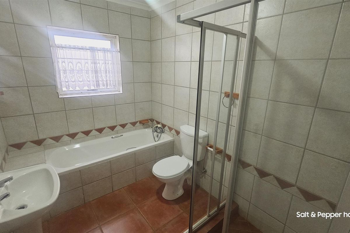 A functional bathroom featuring a bathtub, separate shower enclosure, toilet, and pedestal basin with neutral wall tiling and terracotta floor tiles.