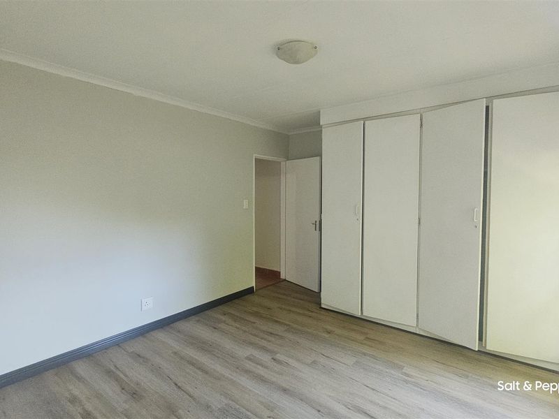 A bright, empty bedroom featuring neutral walls, modern laminate flooring, and ample built-in cupboard storage space.