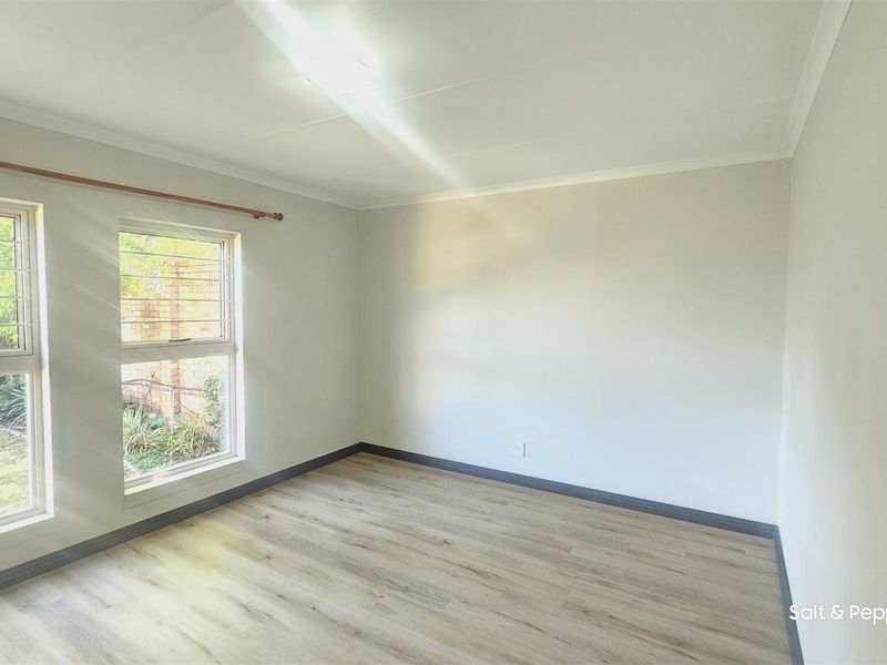 A bright, empty bedroom featuring modern laminate flooring, neutral walls, and windows fitted with security bars.