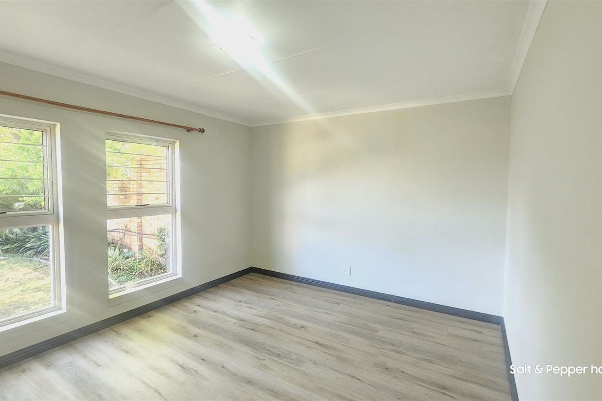 A bright, empty bedroom featuring modern laminate flooring, neutral walls, and windows fitted with security bars.