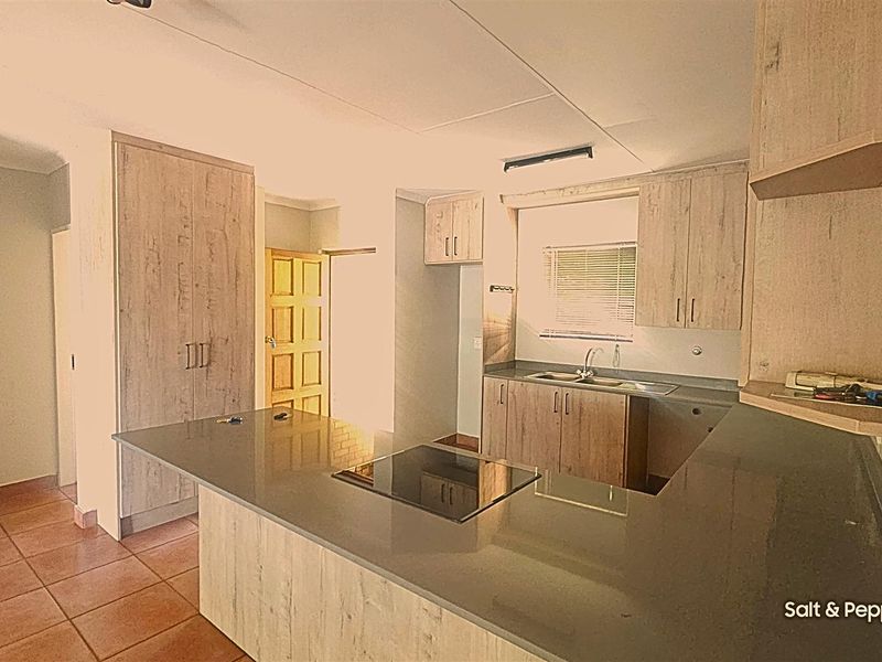 A functional kitchen featuring light wood-grain cabinetry, stone countertops, an integrated hob, and tiled flooring, offering a clean and practical workspace.