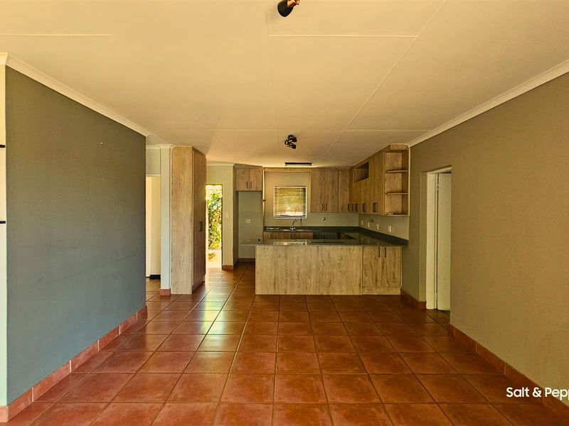 An open-plan living and kitchen area featuring tiled flooring, wood-look cabinetry, and a central kitchen island, offering a functional and versatile layout.