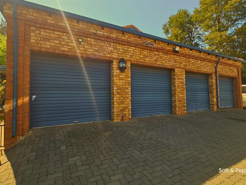A spacious four-car garage featuring a classic brick facade, blue roller shutter doors, and a neatly paved driveway.
