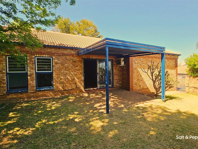 Rear view of the townhouse featuring a brick facade, a paved patio area covered by a blue metal pergola, and a small garden.
