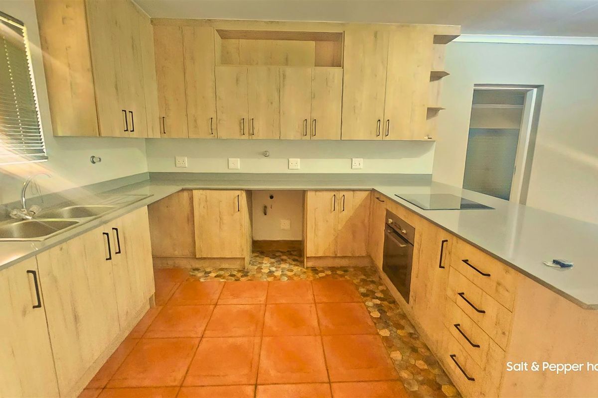 A functional kitchen featuring light wood-look cabinetry, built-in oven, electric hob, and double sink with ample counter space.