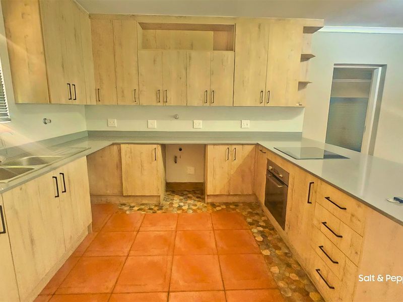A functional kitchen featuring light wood-look cabinetry, built-in oven, electric hob, and double sink with ample counter space.