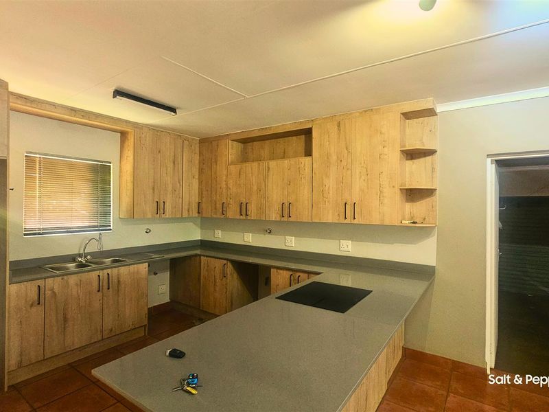 A functional kitchen featuring light wood-finish cabinetry, stone countertops, a double basin sink, and a built-in hob, set against tiled flooring.