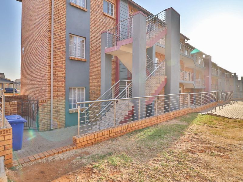 Exterior view of a multi-story apartment complex featuring face brick construction, external staircases with stainless steel railings, and paved ground-level access.