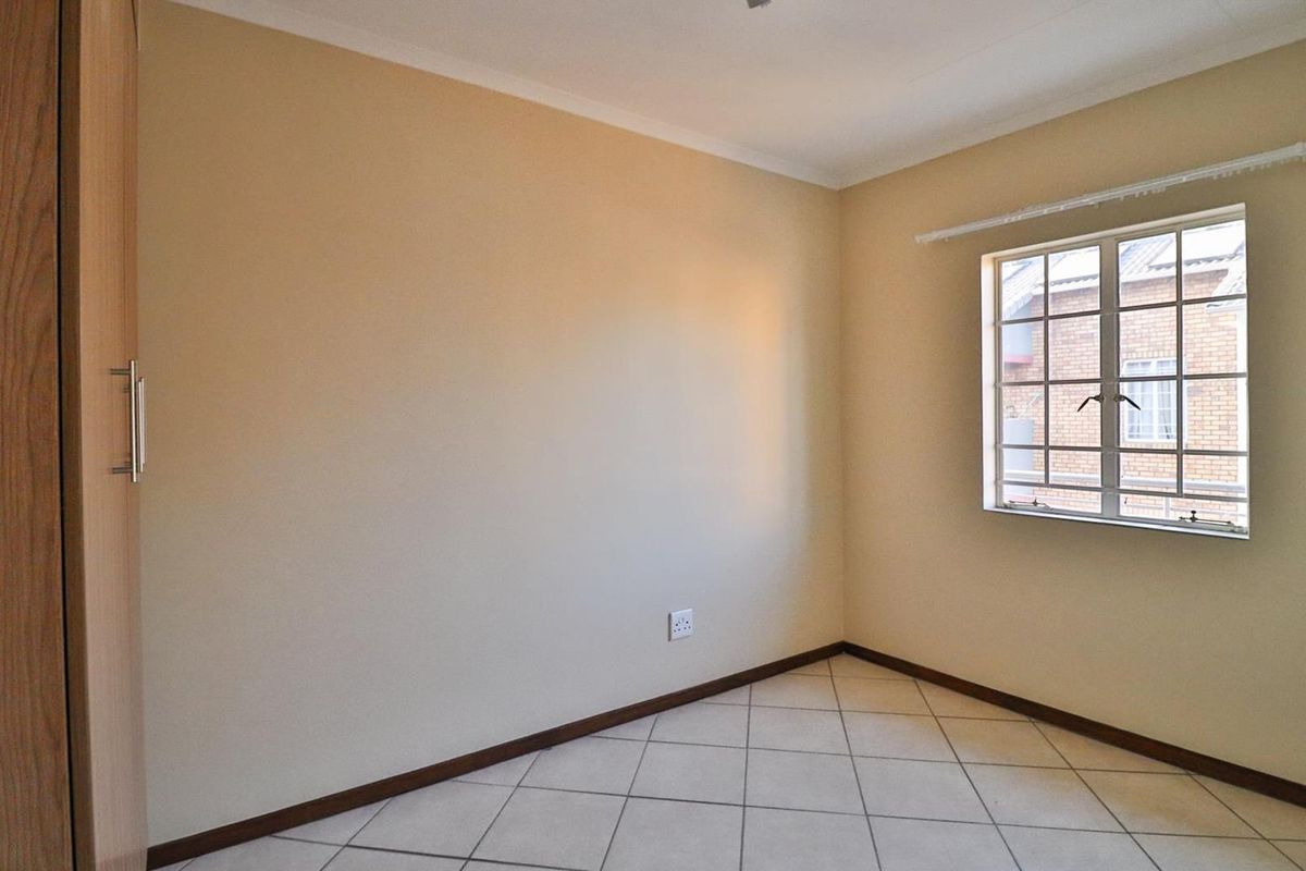 A clean, empty bedroom featuring tiled flooring, a built-in wardrobe, and a window with security bars.