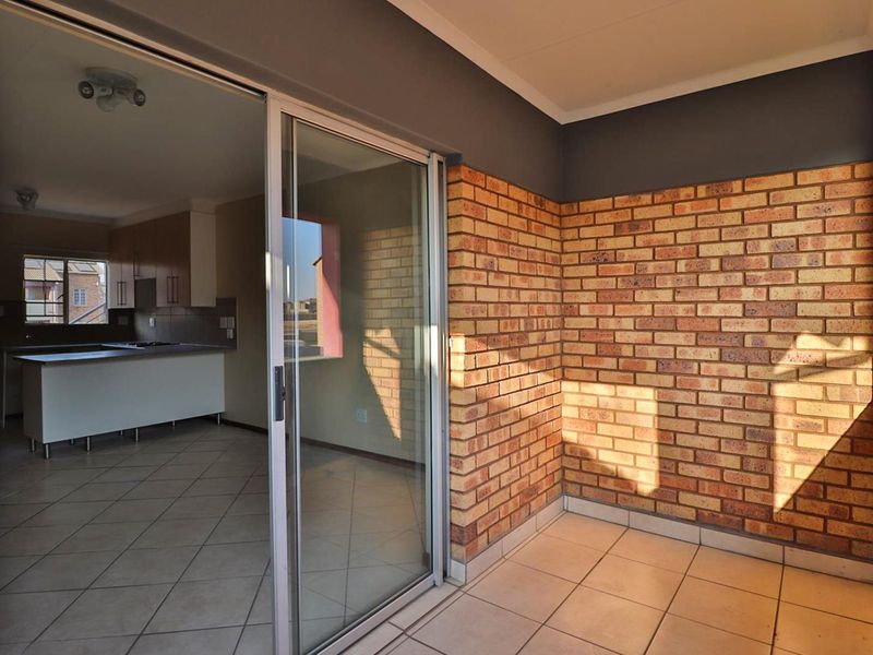 A covered balcony featuring exposed brick walls and tiled flooring, providing direct access to an open-plan kitchen and living area.