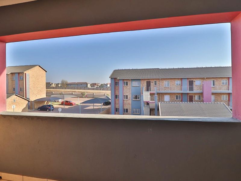 A view from an apartment balcony overlooking the complex grounds, parking area, and neighbouring residential buildings.
