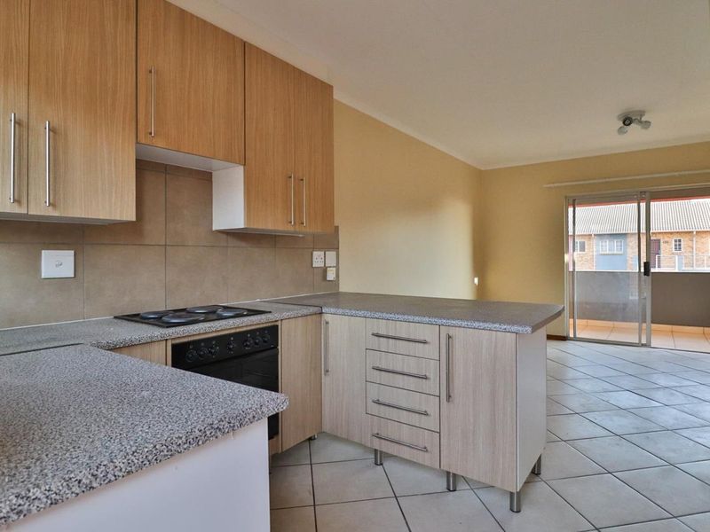 Open-plan kitchen featuring light wood cabinetry, laminate countertops, and built-in appliances, flowing into a living area with access to a private balcony.