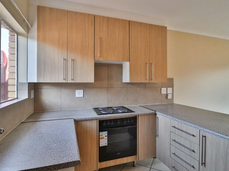 A functional kitchen featuring light wood-finish cabinetry, granite-look laminate countertops, a built-in electric oven and hob, and neutral tiled backsplash.