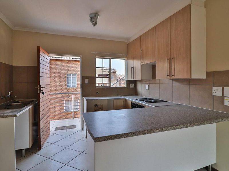 A functional kitchen featuring built-in cabinetry, laminate countertops, a hob, and tiled flooring, with direct access to an outdoor balcony area.