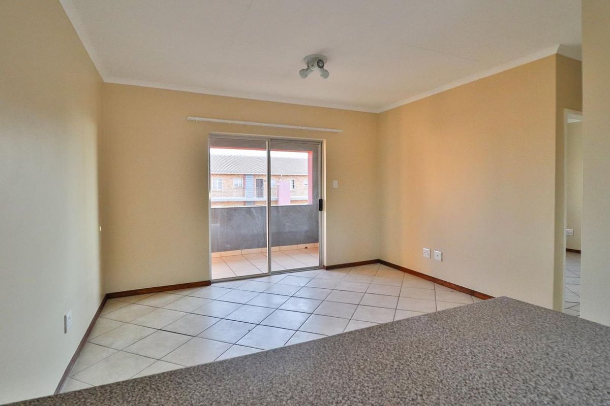 An empty open-plan living area featuring tiled flooring, neutral walls, and a sliding glass door providing access to an outdoor balcony.