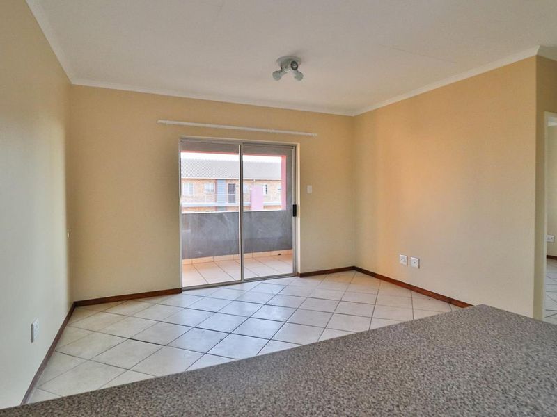 An empty open-plan living area featuring tiled flooring, neutral walls, and a sliding glass door providing access to an outdoor balcony.