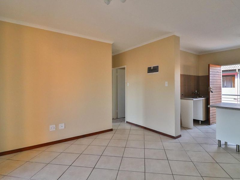 An open-plan living and kitchen area featuring tiled flooring, neutral walls, and a functional kitchen layout with a breakfast counter.
