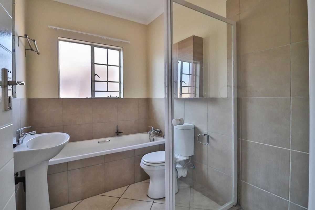 A functional bathroom featuring a pedestal basin, bathtub, and a separate shower enclosure with neutral wall and floor tiling.