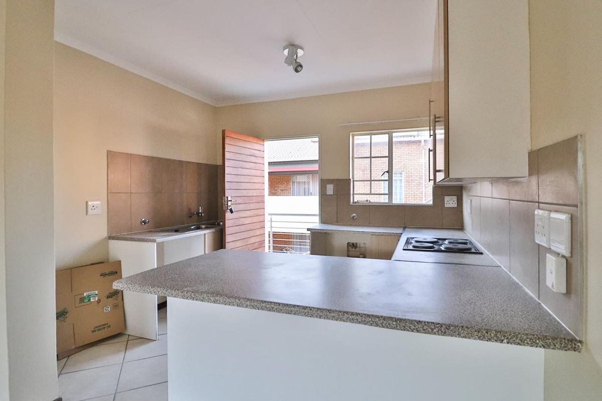 A functional kitchen featuring built-in cabinetry, laminate countertops, an electric hob, and tiled splashbacks, currently vacant and awaiting finishing touches.