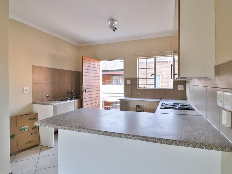 A functional kitchen featuring built-in cabinetry, laminate countertops, an electric hob, and tiled splashbacks, currently vacant and awaiting finishing touches.
