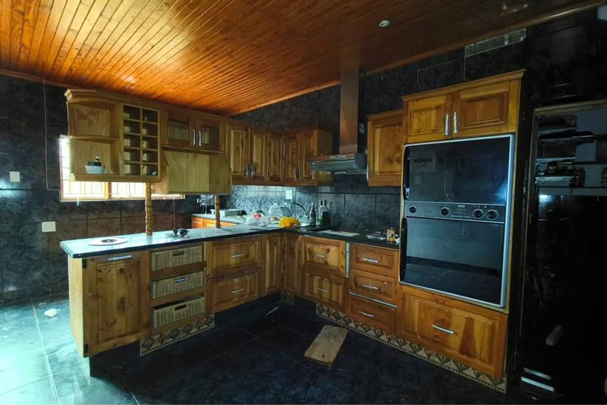 A traditional kitchen featuring solid wood cabinetry, dark tiled flooring, a built-in double oven, and a distinctive wood-paneled ceiling.