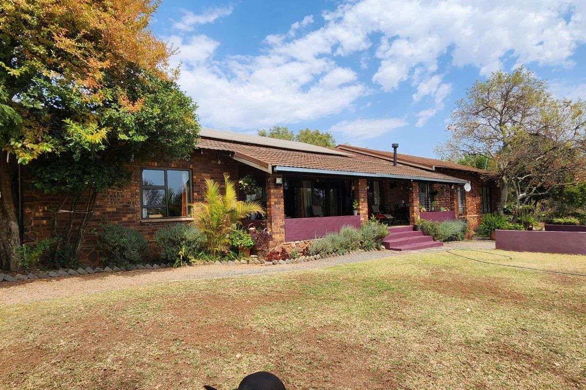 A view of the rear brick farmhouse elevation featuring a covered patio, attached carport, and established garden surroundings.