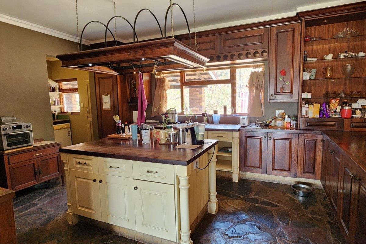A rustic-style kitchen featuring dark wood cabinetry, a central kitchen island with a wooden countertop, stone flooring, and an overhead pot rack.