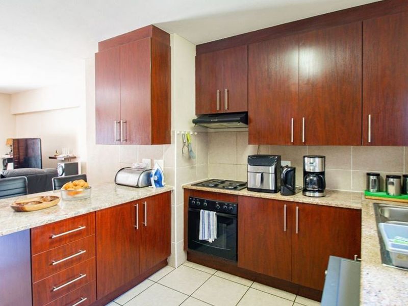 Open-plan kitchen featuring dark wood cabinetry, granite countertops, built-in oven, and gas hob, seamlessly flowing into the adjacent living area.