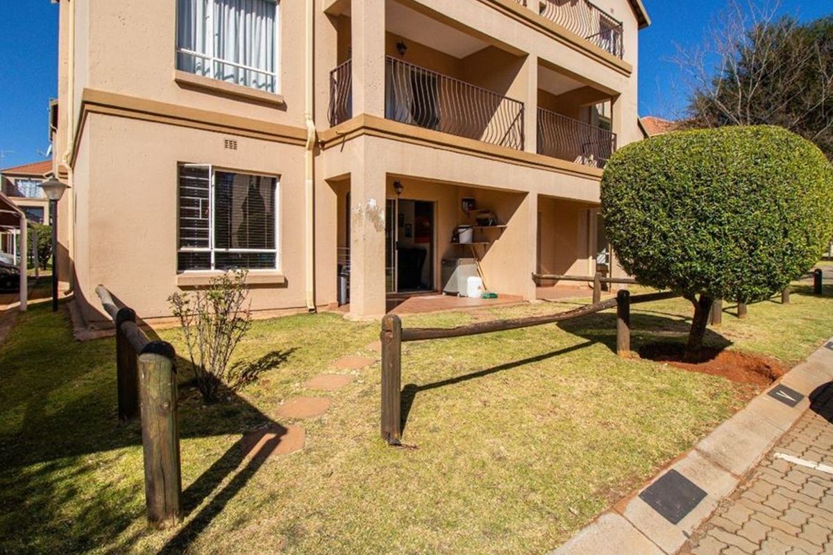 Exterior view of an apartment building featuring a ground-floor patio, balcony above, and a small private garden area with timber fencing.