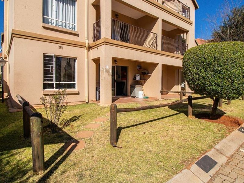 Exterior view of an apartment building featuring a ground-floor patio, balcony above, and a small private garden area with timber fencing.