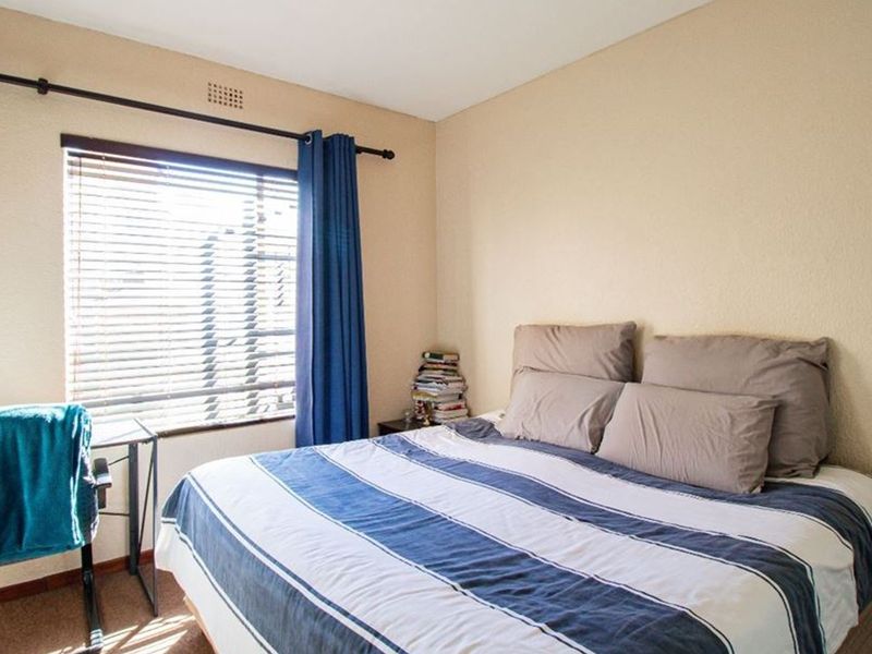 A functional bedroom featuring a window with venetian blinds and a ventilation grille, providing natural light and airflow.