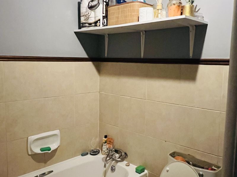 A functional bathroom featuring a bathtub, toilet, and wall-mounted shelving with tiled wall finishes.