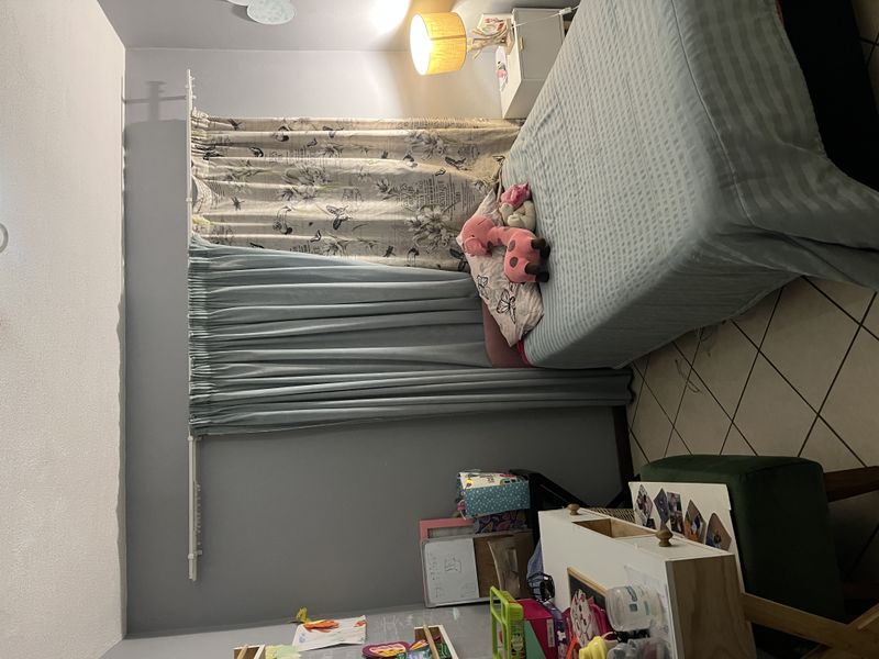 A bedroom featuring tiled flooring and a wall-mounted curtain rod, currently utilized as a child's room.