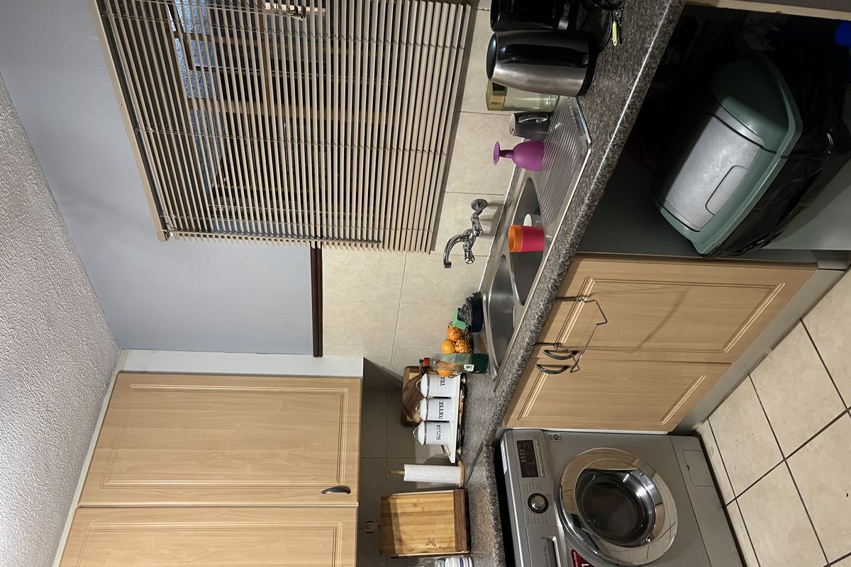 A functional kitchen featuring light wood-finish cabinetry, a double stainless steel sink, tiled backsplash, and integrated washing machine space.
