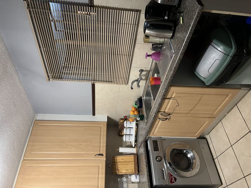 A functional kitchen featuring light wood-finish cabinetry, a double stainless steel sink, tiled backsplash, and integrated washing machine space.