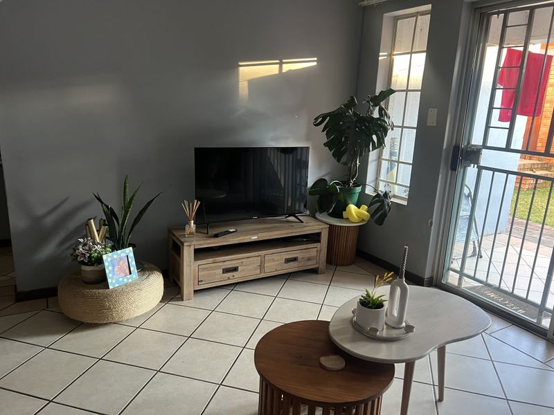 A living room area featuring tiled flooring, a sliding glass door with a security gate, and natural light from a side window.