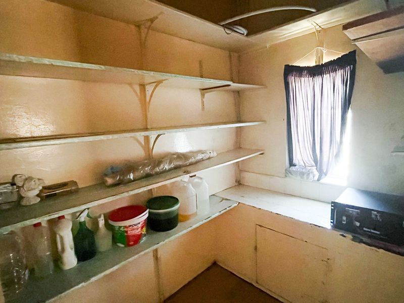 A functional scullery or pantry area featuring built-in shelving and counter space, requiring cosmetic updates to improve its overall condition and utility.