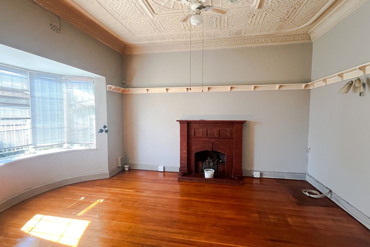 Spacious living room featuring original pressed metal ceilings, a classic timber fireplace, bay window, and polished hardwood flooring.