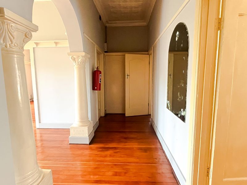 A spacious hallway featuring classic architectural details including decorative columns, an elegant archway, polished hardwood flooring, and a traditional pressed metal ceiling.