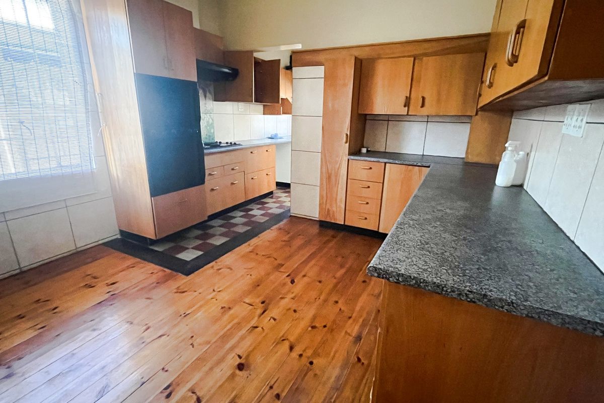 A functional kitchen featuring wooden cabinetry, laminate countertops, built-in oven, extractor fan, and tiled backsplash with wooden flooring.
