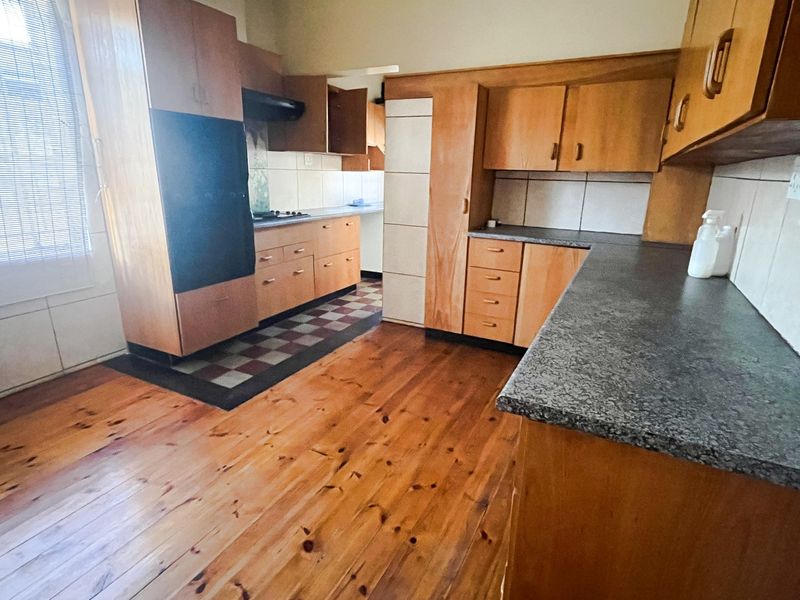A functional kitchen featuring wooden cabinetry, laminate countertops, built-in oven, extractor fan, and tiled backsplash with wooden flooring.