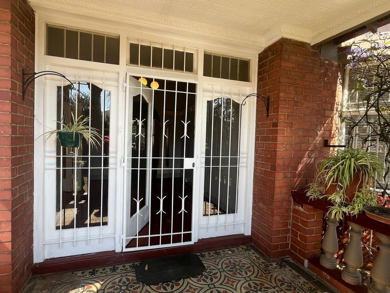 A charming covered front porch featuring classic exposed brickwork, decorative period floor tiles, and a secure entrance gate.