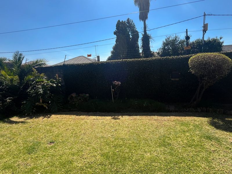 A private backyard garden featuring a well-maintained lawn, established perimeter wall, and integrated electric security fencing.